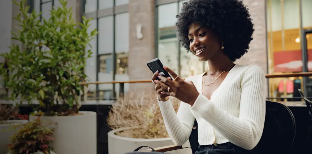 A smiling woman paying on her phone at a café terrace